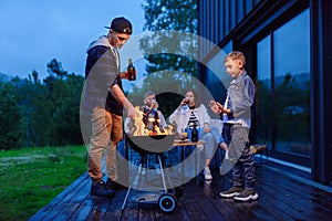 Happy father and son preparing a barbecue on a family vacation on the terrace of their modern house in the evening.