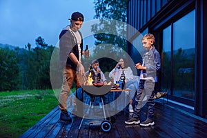 Happy father and son preparing a barbecue on a family vacation on the terrace of their modern house in the evening.