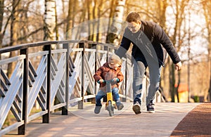 Happy father and son ride a bicycle on a bridge on a sunny day.