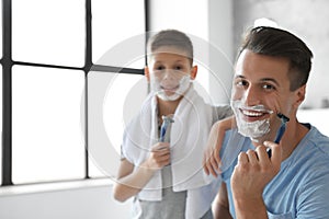 Happy father and son with shaving foam on their faces in bathroom