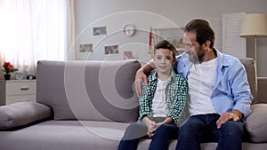 Happy father and son sitting on coach at home, family relationship, closeness photo
