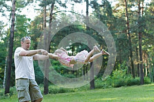 Happy father spinning around his daughter in green summer park outdoors