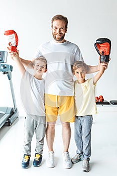 happy father standing with sons in boxing gloves raising hands