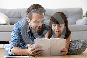 Happy father and surprised kid girl reading book together