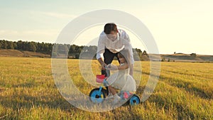 Happy father teaches little daughter to ride a bike. Dad plays with small child on lawn. kid learns to ride bicycle