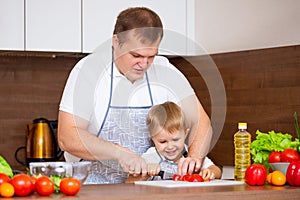 Happy father teaches son to cut salad in the kitchen