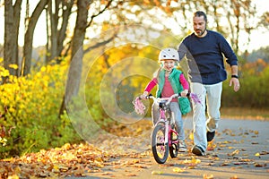 Happy father teaching his little daughter to ride a bicycle. Child learning to ride a bike.