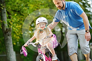 Happy father teaching his little daughter to ride a bicycle. Child learning to ride a bike.