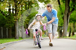 Happy father teaching his little daughter to ride a bicycle. Child learning to ride a bike.