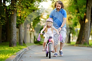 Happy father teaching his little daughter to ride a bicycle. Child learning to ride a bike.