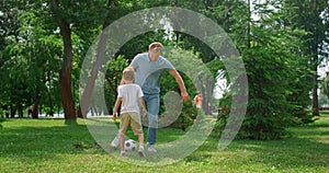 Happy father teaching son play soccer. Cheerful boy passing ball to dad on lawn.