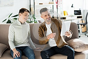 Happy father and teen son using tablet on sofa