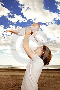 Happy father throws up baby boy against blue sky