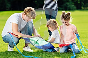 happy father with two children playing with kite on green grass