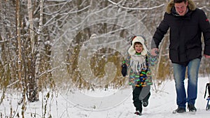 Happy father and a very cute happy little boy, his son runs in a snow winter park. smiling boy. Attractive family having