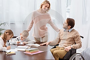 happy father on wheelchair and mother teaching children