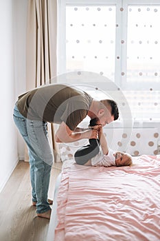 Happy father young man and baby girl little daughter having fun on bed in room at home