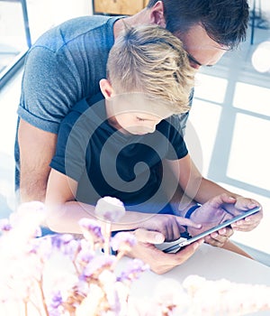 Happy father with young son using tablet PC in sunny room.Dad and little boy playing computer resting indoor together.Vertical, bl