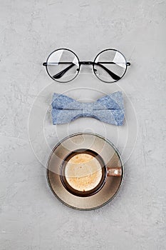 Happy Fathers Day background with morning coffee mug, glasses and bowtie on stone gray table top view in flat lay style.