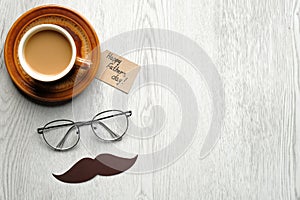 Happy Fathers Day concept. Cup of coffee, label with text Happy Father`s Day, glasses and mustache on wooden table. Flat lay, top