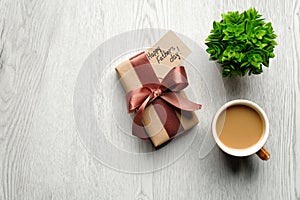 Happy Fathers Day concept. Gift box with label Happy Father`s Day, cup of coffee and plant on wooden table. Flat lay, top view