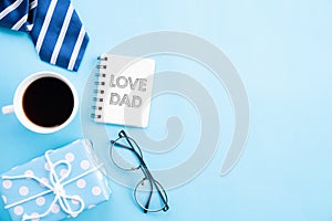 Happy fathers day concept. Top view of blue tie, beautiful gift box, coffee mug, glasses with LOVE DAD text on bright blue pastel
