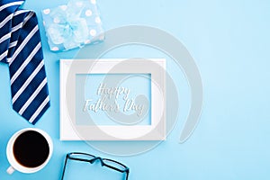 Happy fathers day concept. Top view of blue tie, beautiful gift box, coffee mug, white picture frame with happy father`s day text