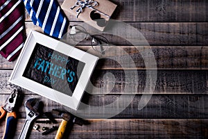 Happy fathers day concept. Top view of white picture frame with border of tools and ties, retro f glasses on dark wooden table