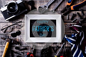 Happy fathers day concept. Top view of white picture frame with border of tools and ties, retro film camera on dark wooden table