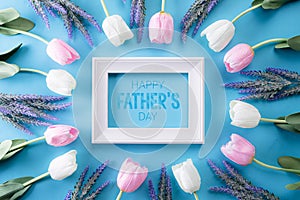 Happy fathers day concept. Top view of white pink tulip flowers and picture frame with Happy father`s day text on bright blue