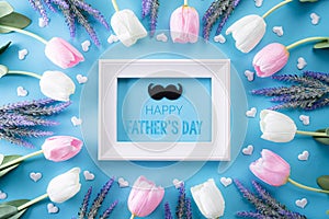 Happy fathers day concept. Top view of white pink tulip flowers and picture frame with Happy father`s day text on bright blue