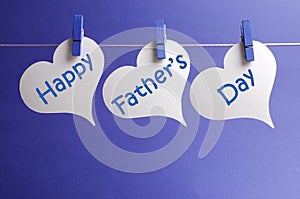 Happy Fathers Day message written on white heart shape tags hanging from blue pegs on a line