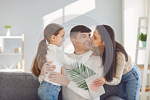 Happy fathers day. Mother and child daughter congratulates dad with a postcard in a room with a window.