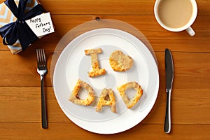 Happy Fathers Day table setting concept. Father`s Day brunch with homemade bakery I love Dad on plate, gift box, cup of coffee on