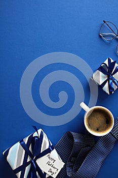 Happy Fathers Day vertical banner design. Flat lay gift boxes, coffee cup, glasses, necktie on dark blue background