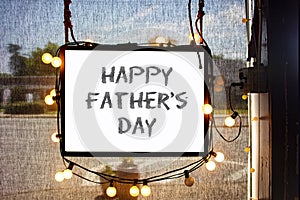 Happy Fathers Day written on hanging sign surrounded by party lights in shop window with semi-transparent dark solar shades behind