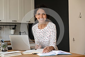 Happy female adult student with laptop and notebooks studying online