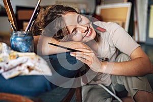 Happy female artist smiling and resting with closed eyes in her art studio. A joyful woman painter falling asleep in her workshop
