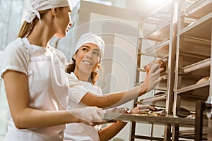 happy female bakers putting fresh pastry on shelves