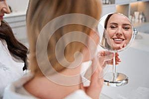 Happy female blonde looks inirror at consultation with esthetician