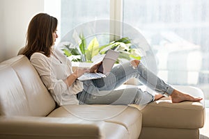Happy female browsing internet sitting on sofa at home