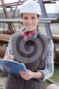 happy female builder writing on clipboard outdoors