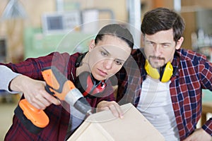 happy female carpenter drilling wood while colleague working in background