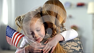 Happy female child with flag of USA hugging military hero mother, patriotism