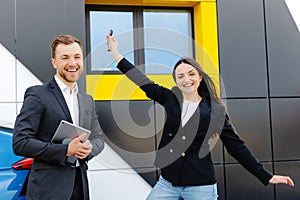 Happy female client standing at brand new car and taking keys from dealer in dealership outdoor. The woman is very happy with the