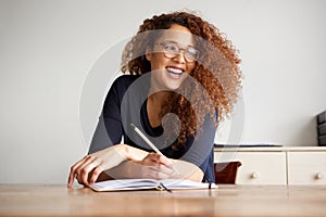 Happy female college student sitting at desk writing in book
