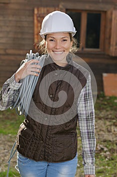 Happy female construction worker carrying wires