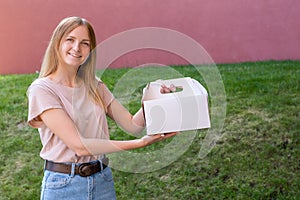 Happy female courier holding dessert in unmarked cardboard box. Delivery service concept. Advertising area.