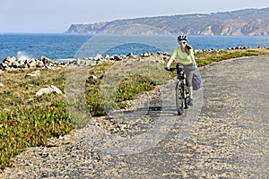 Happy female cyclist rides bicycle on road along ocean shore.