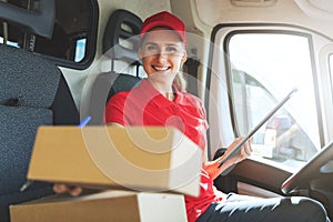 happy female delivery service worker sitting in van and delivering a box
